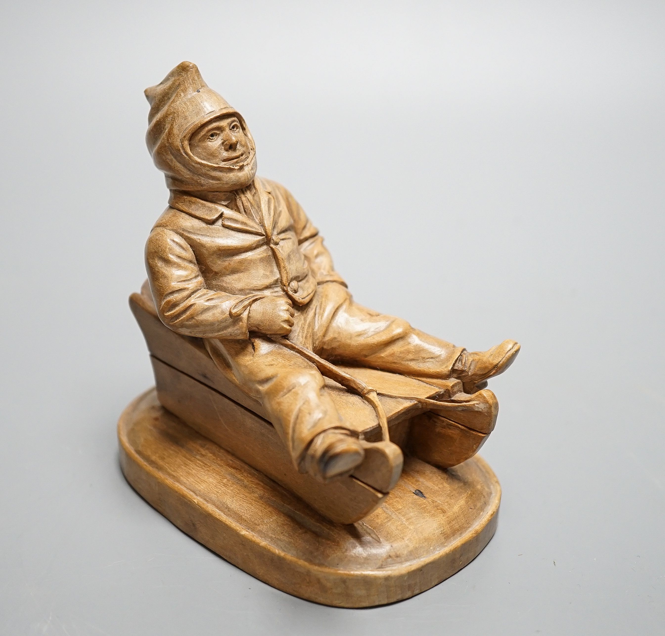 A North European novelty carved beech inkwell in the form of a seated figure sledging, c.1900, 11cm high, 11cm long.